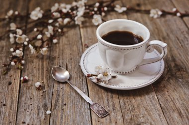 Чашка кофе на блюдце с ветками цветущей вишни на деревянной поверхности