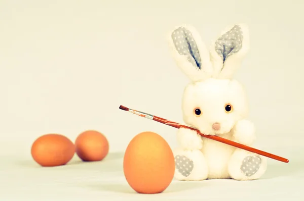 Coelho de brinquedo com ovos e pincel de pintura — Fotografia de Stock