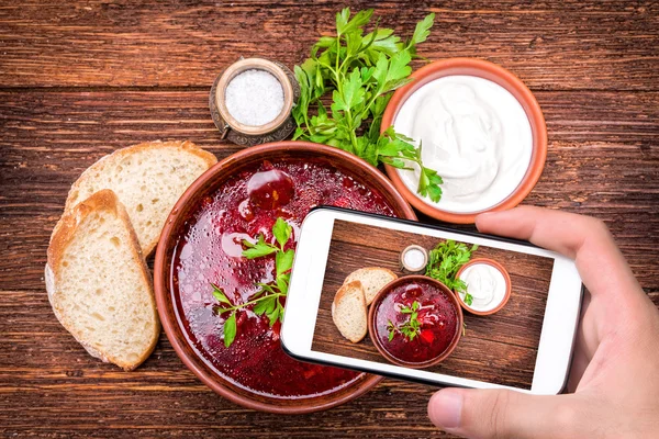 Mãos tirando foto sopa de beterraba vermelha com smartphone . — Fotografia de Stock