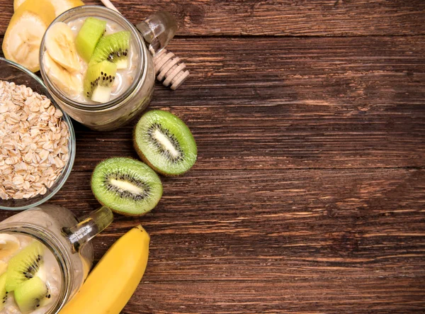 Smoothies aux flocons d'avoine, banane, kiwi en pots de verre sur fond de bois . — Photo