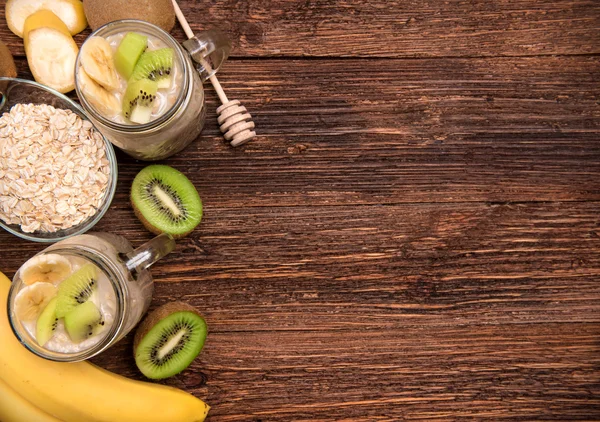 Frullati con farina d'avena, banana, kiwi in vasetti di vetro su fondo di legno . — Foto Stock