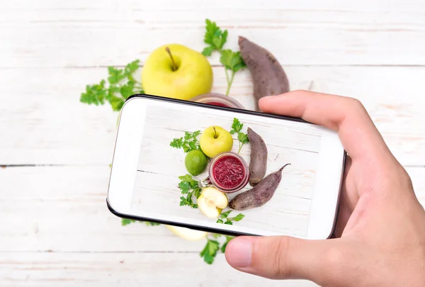 Manos tomando batidos fotográficos con remolacha, manzana, limón, perejil con smartphone . — Foto de Stock