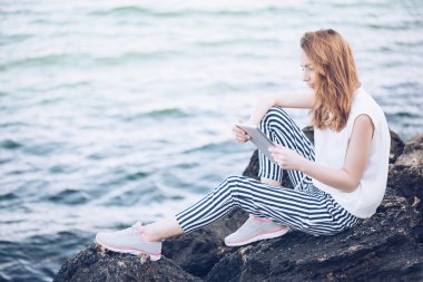 Deniz kenarında bir dijital tablet kullanan kız.