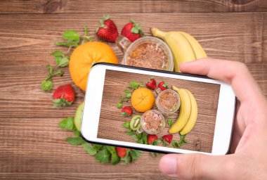 Eller fotoğraf tatlı meyve ve yoğurt ile smartphone ile cam alarak.