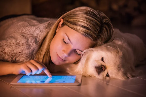 Ung flicka vilar med en hund hemma och använder tablett . — Stockfoto