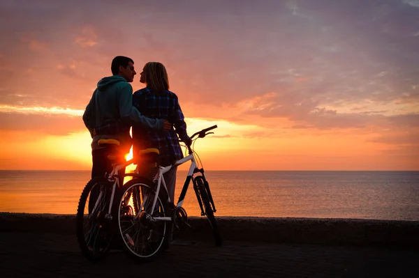 Par av cyklister på stranden vid solnedgången. — Stockfoto