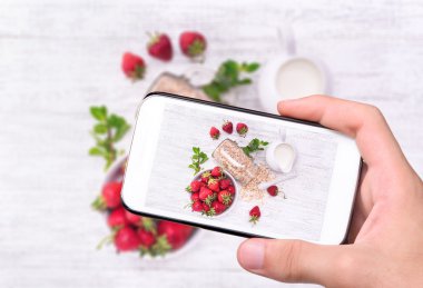 Yulaf ezmesi, çilek cam ile smartphone ile fotoğraf smoothies alarak eller.