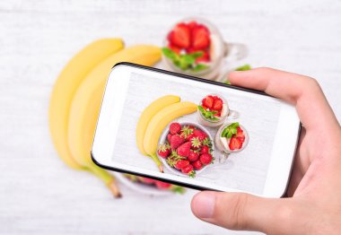 Eller fotoğraf smoothies yulaf ezmesi, çilek, muz ile smartphone ile cam alarak.