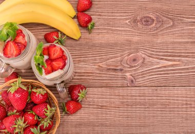 Yulaf ezmesi, çilek, muz ahşap arka plan üzerinde cam kavanozlara smoothies.