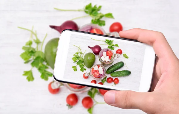 Manos tomando ensalada de tomate con pepino y feta con smartphone . —  Fotos de Stock