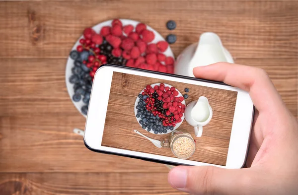 Hands taking photo smoothies with oatmeal ,berries in glass with smartphone. — Stock Photo, Image