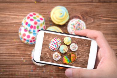 Fotoğrafta el smartphone ile cupcakes renkli.