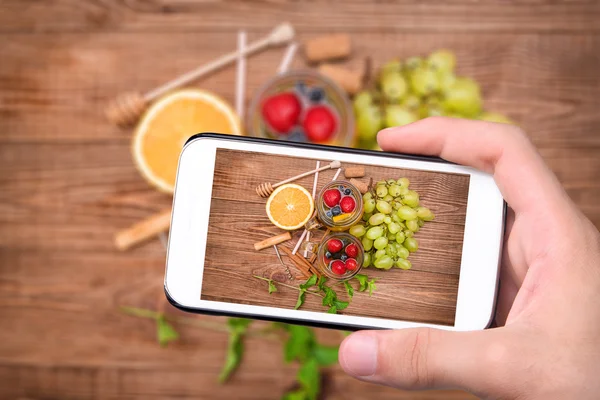 Handen nemen foto witte wijn sangria met verse bessen met smartphone. — Stockfoto