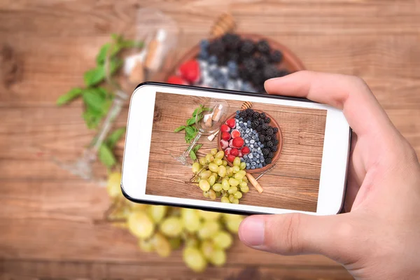 Handen nemen foto witte wijn sangria met verse bessen met smartphone. — Stockfoto