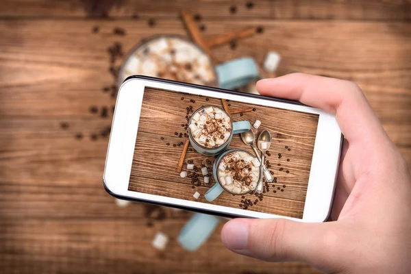 Mãos tirando foto xícara de cacau com marshmallows e chocolate com smartphone . — Fotografia de Stock