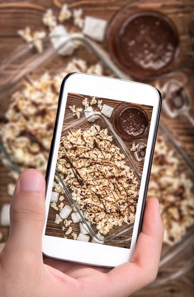 Mãos tirando foto pipoca de caramelo de chocolate escuro com smartphone . — Fotografia de Stock