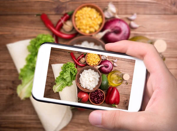 Mãos tirando foto burrito vegetariano mexicano caseiro com smartphone . — Fotografia de Stock