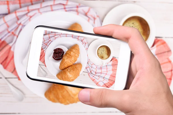 Mãos tirando foto xícara de café com croissants com smartphone — Fotografia de Stock