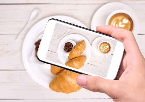 Ruce s Foto šálek kávy s croissanty s smartphone — Stock fotografie