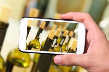 Eller fotoğraf şarap şişeleri ile smartphone alarak.
