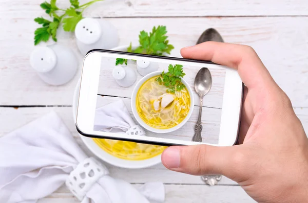 Manos tomando sopa de fideos de pollo con teléfono inteligente . — Foto de Stock