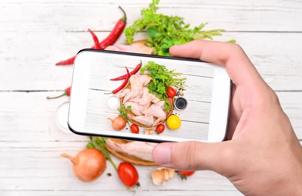 Mani che scattano foto ali di pollo crudo con smartphone . — Foto Stock