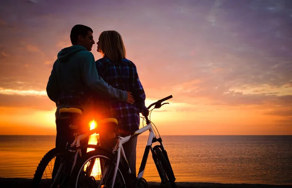 Par av cyklister på stranden vid solnedgången. — Stockfoto