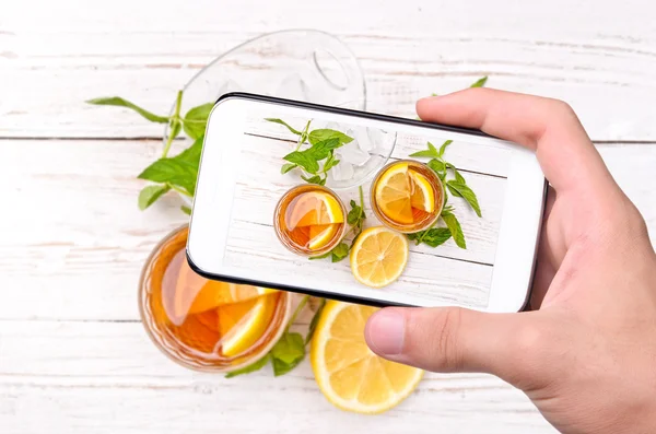 Mani che scattano foto tè freddo con limone con smartphone . — Foto Stock
