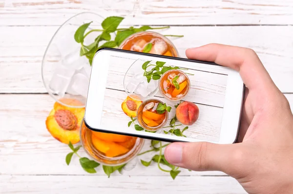 Ręce przy zdjęcie lodu herbaty z brzoskwinią z smartphone. — Zdjęcie stockowe