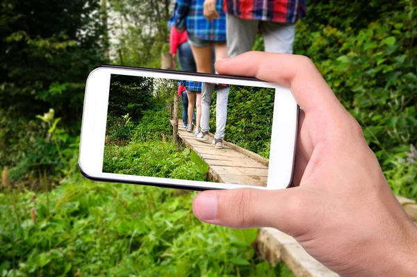 Mãos tirando foto turistas andando em uma ponte de madeira com smartphone . — Fotografia de Stock