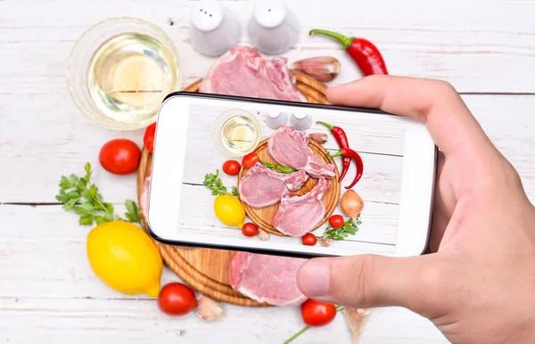 Mãos tirando foto carne de costelas crua com smartphone . — Fotografia de Stock