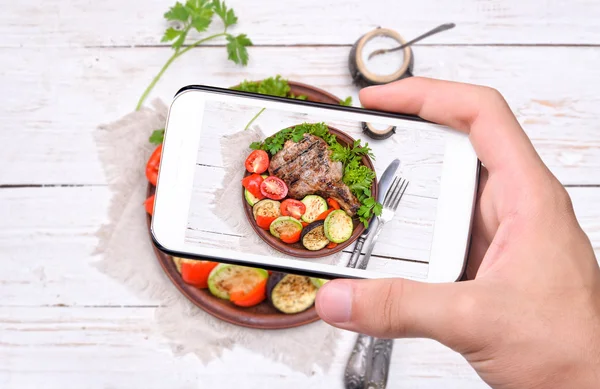 Manos tomando foto costilla a la parrilla con verduras a la parrilla con smartphone . —  Fotos de Stock