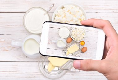 Eller fotoğraf süt ve süt ürünleri ile smartphone alarak.