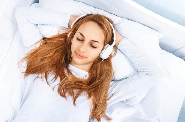 Chica en la cama con auriculares al escuchar la música — Foto de Stock