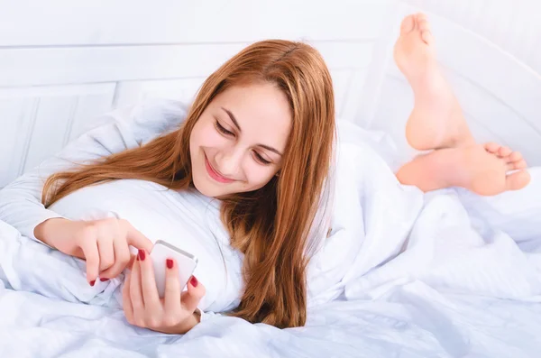 Chica en la cama con teléfono celular — Foto de Stock