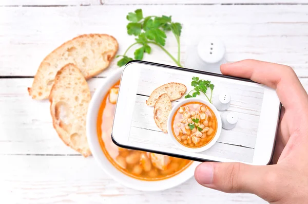 Руки делают фото бобовый суп со смартфоном . — стоковое фото