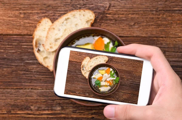 Ruce s Foto polévka s kuřetem a zeleninou s smartphone. — Stock fotografie