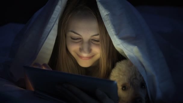Lány az ágyon tabletta kutyájával. — Stock videók