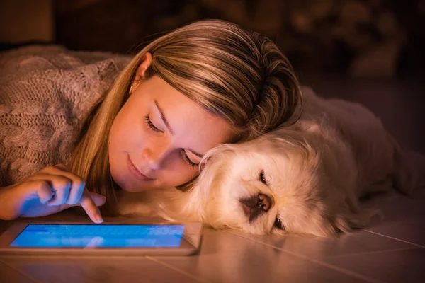 Gadis muda sedang beristirahat dengan anjing di rumah dan menggunakan tablet . — Stok Foto