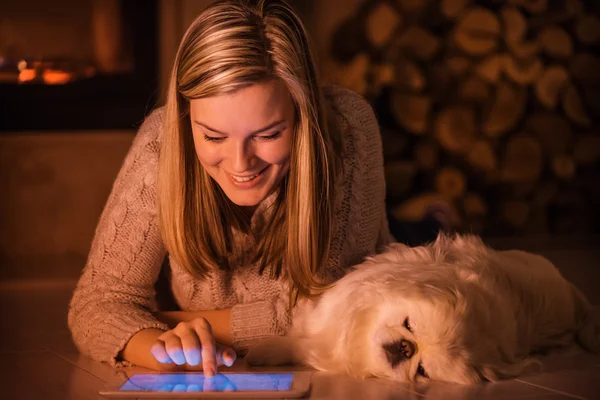 Ung flicka vilar med en hund hemma och använder tablett . — Stockfoto