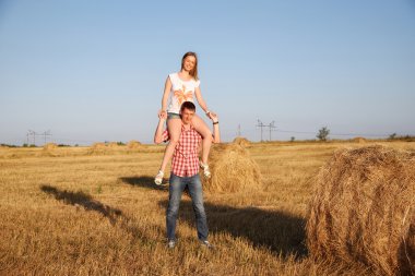 Genç erkek ve kadın bir balya saman hasat bir tarlada olarak eğleniyor.