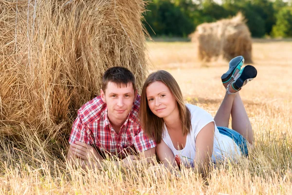 Jovem homem e mulher posando em um campo perto de um fardo de feno — Fotografia de Stock