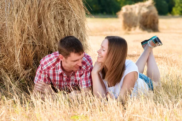 Jeune homme et femme posant dans un champ près d'une balle de foin — Photo
