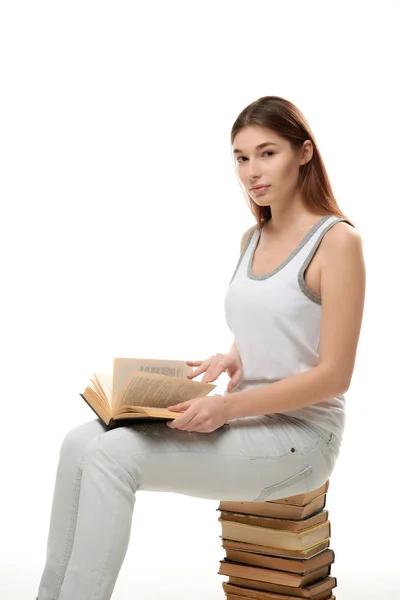 Una joven se sienta en una pila de libros. Mantiene el libro en su regazo . —  Fotos de Stock