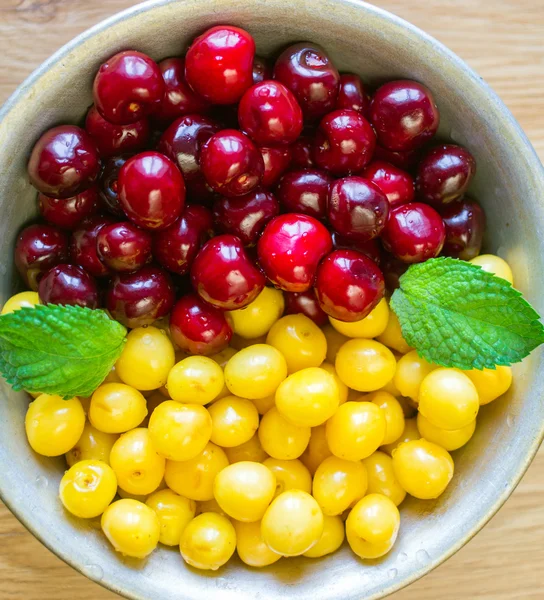 Em uma tigela as cerejas doces e as folhinhas de casa da moeda mentem . — Fotografia de Stock