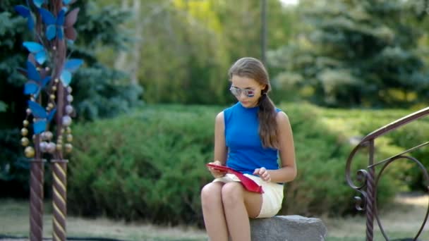 Ragazza nel parco si siede su una roccia e leggere e-book . — Video Stock