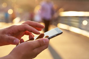 Adam cep telefonunu açık havada kullanıyor, kapat. Erkekler dışarıda cep telefonu kullanarak mesajlaşırken el ele tutuşuyorlar.