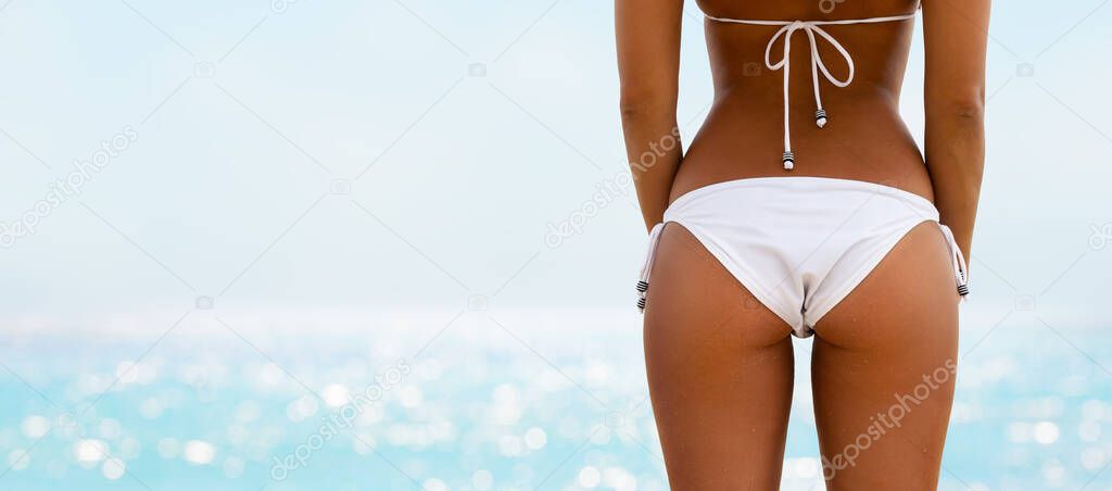 Beautiful young girl with bronze tan on the beach in a white bikini. Close-up of beautiful woman in a swimsuit posing on the beach. Summer beach concept.