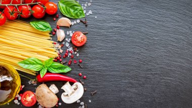 Gıda malzemeleri koyu arka planda. Domates, spagetti, baharat, sarımsak ve fesleğen yaprağı. İtalyan yemekleri, sağlık veya yemek pişirme konsepti.