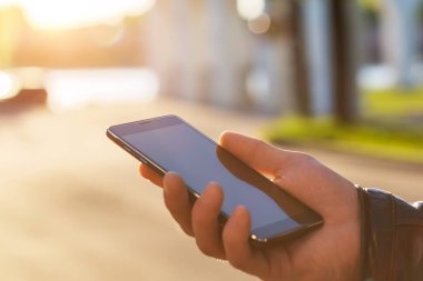 Adam cep telefonunu açık havada kullanıyor, kapat. Erkekler dışarıda cep telefonu kullanarak mesajlaşırken el ele tutuşuyorlar.